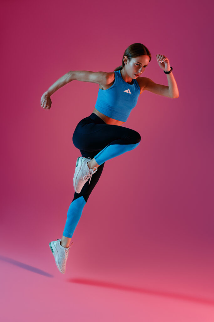 Determined sporty woman running in Mid-Air exercising during cardio workout over studio background