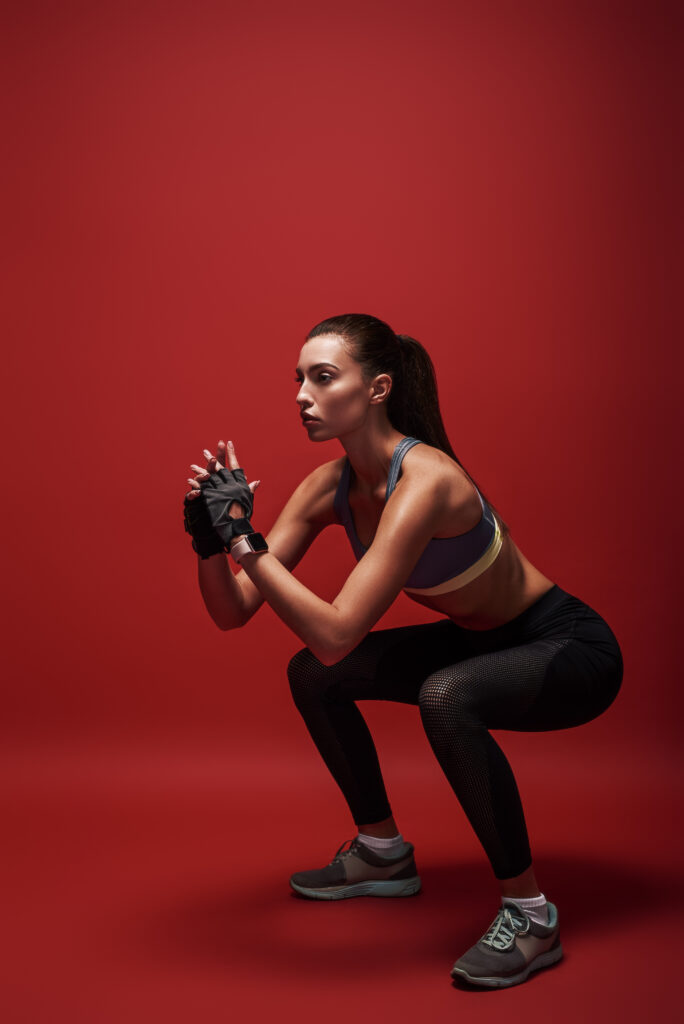 Sport is the way of her life. Sportswomanstanding over red background, stretching her body